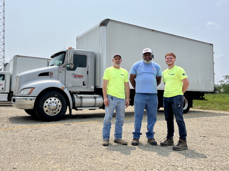 Three Redkey Express employees standing in front of one of their branded vehicles.