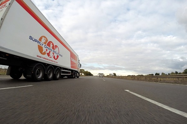 A delivery truck driving on a freeway, featuring the company's logo on the side.