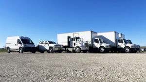 Several vehicles which makes up part of the fleet of Redkey Express trucks, on gravel, shown under a bright blue sky.